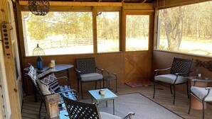 A covered outdoor seating area with wooden flooring, metal chairs, a table, and a hanging light fixture. - Shawnee Creek Hideaway - Close to Eminence and the Jacks Fork River! (Winona)