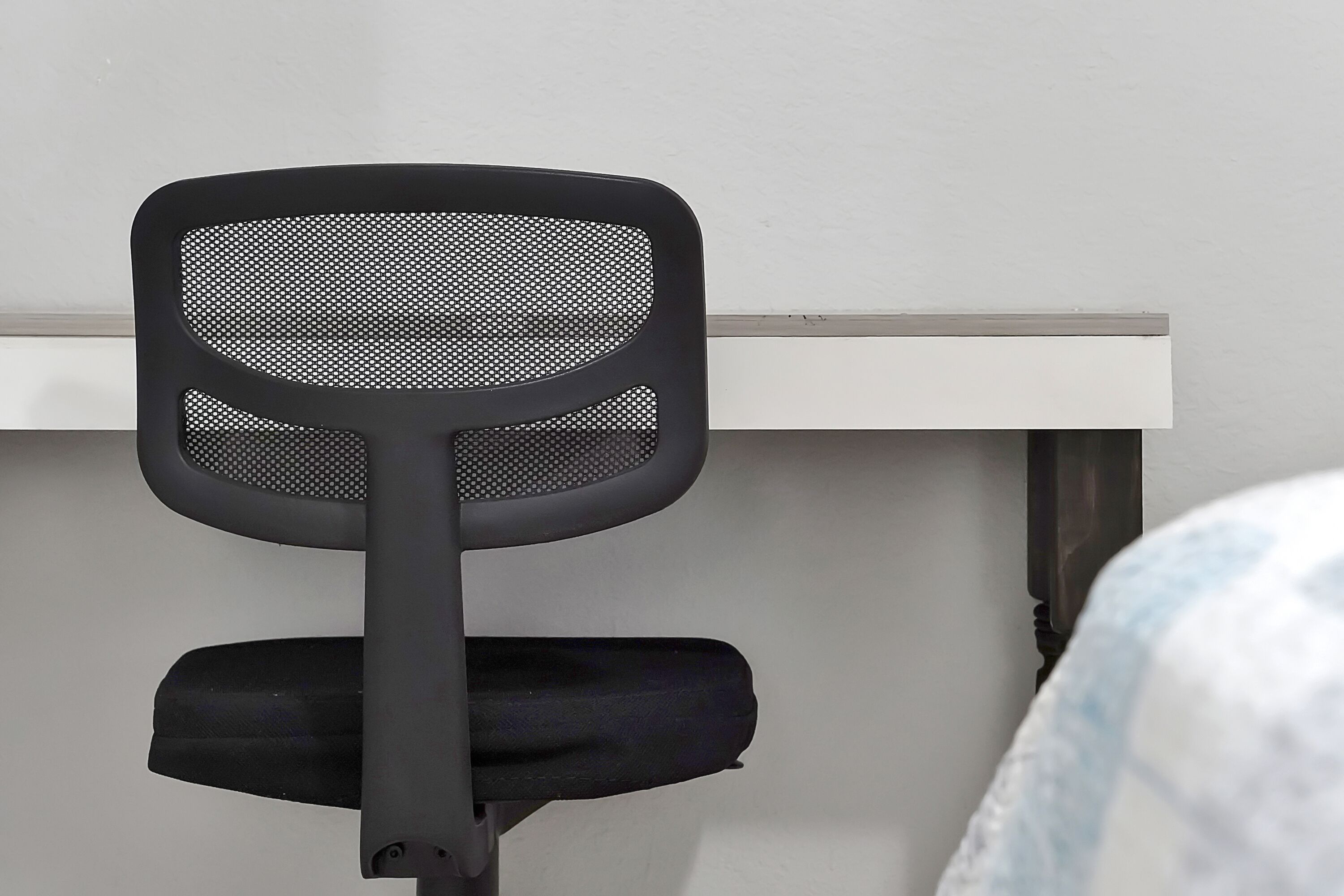 Una silla de oficina negra con respaldo de malla y asiento negro, ubicada frente a un escritorio blanco.