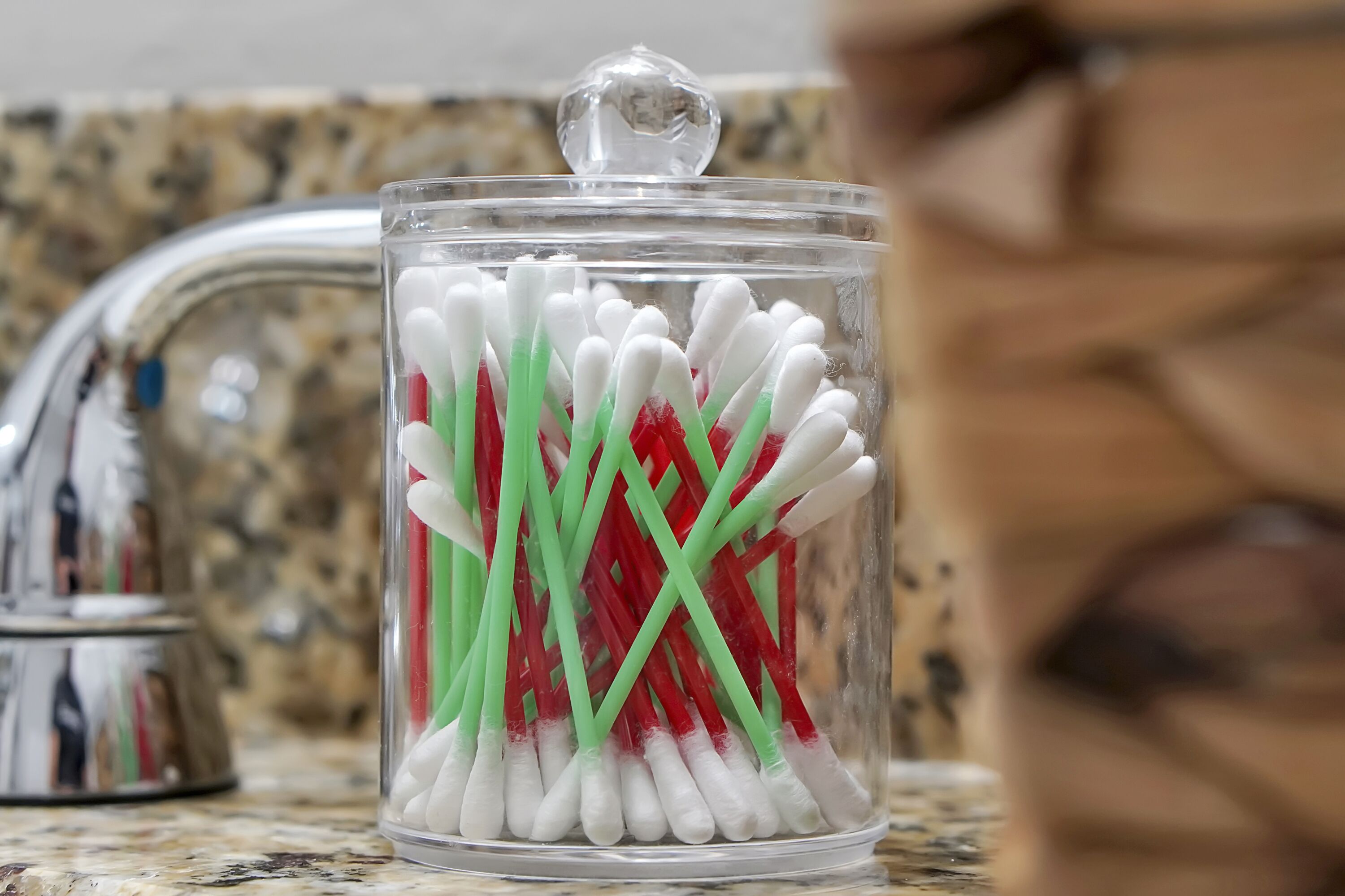 A clear glass container with white and green toothbrushes on a kitchen counter.