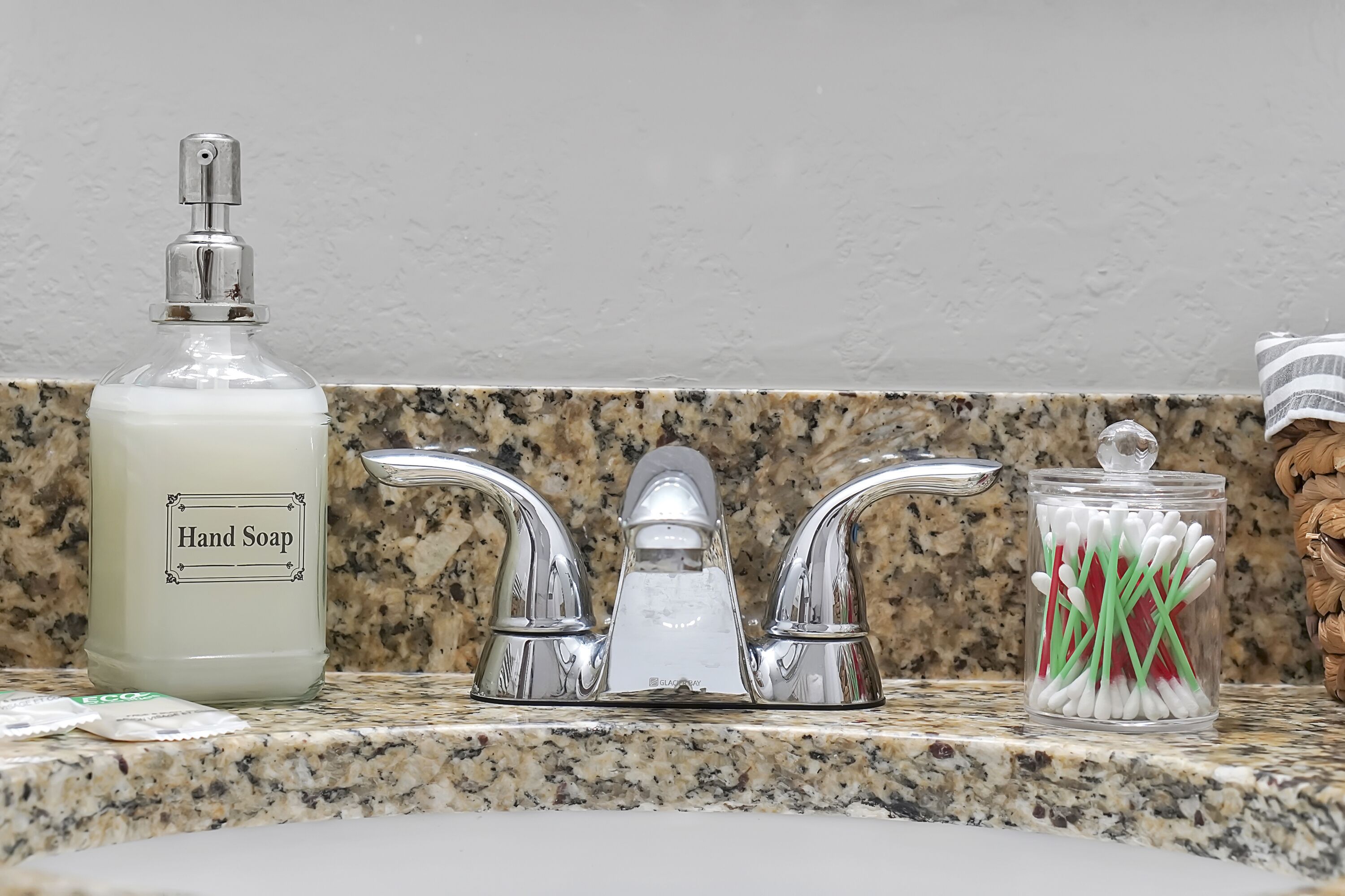 A bathroom sink with a hand soap dispenser, a faucet, and a container of cotton swabs.