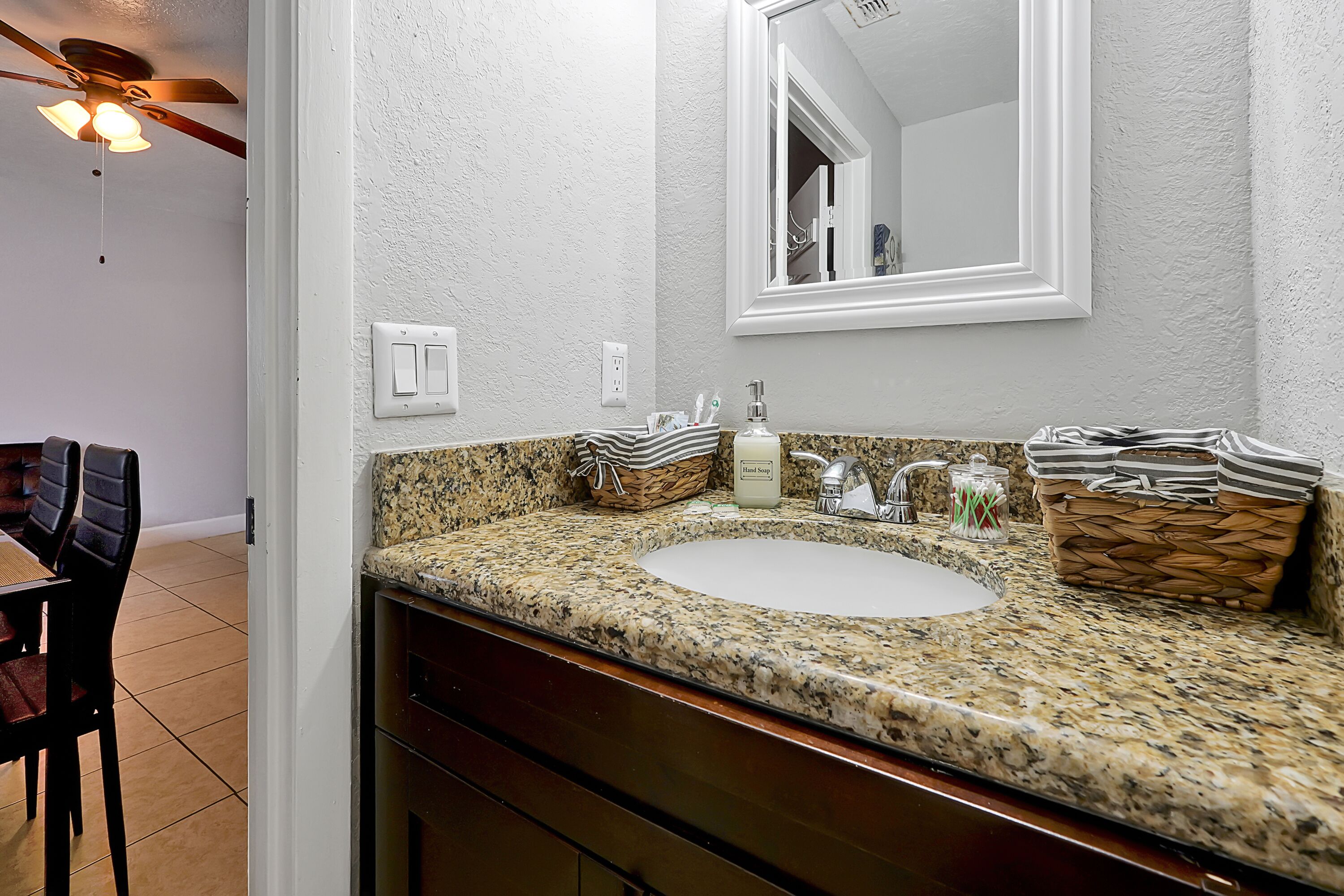 Une salle de bain avec un comptoir en granit, un lavabo blanc, un miroir et un ventilateur de plafond.