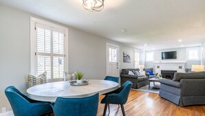Un salon moderne avec une cheminée, un coin repas avec une table ronde et des chaises bleues, et un canapé gris.