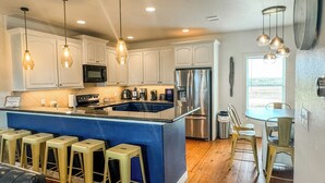 A modern kitchen with white cabinets, stainless steel appliances, and a blue island with bar stools. - Family Beach House near Crystal Beach (Gilchrist) · Walk to the Gulf · Hot Tub (Gilchrist)