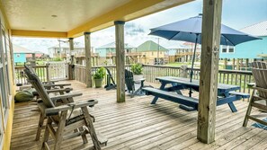 Une terrasse en bois, agrémentée de tables et de chaises pour pique-nique, entourée d’une balustrade en bois, et offrant une vue sur un quartier résidentiel.