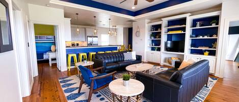 A modern living room with a black leather sofa, a round coffee table, and a blue patterned rug.