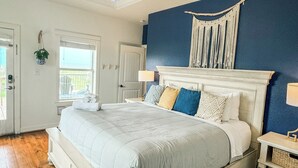 A bedroom with a large bed, a nightstand, a wall-mounted macrame piece, and a window with a view. - Family Beach House near Crystal Beach (Gilchrist) · Walk to the Gulf · Hot Tub (Gilchrist)