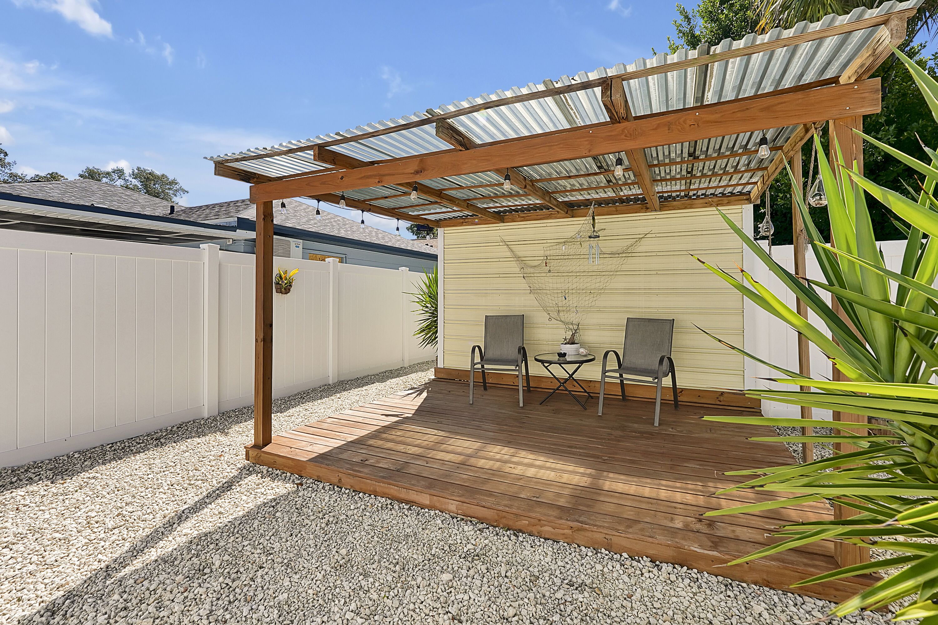 Eine überdachte Terrasse mit Holzdeck, zwei Stühlen und einem kleinen Tisch.
