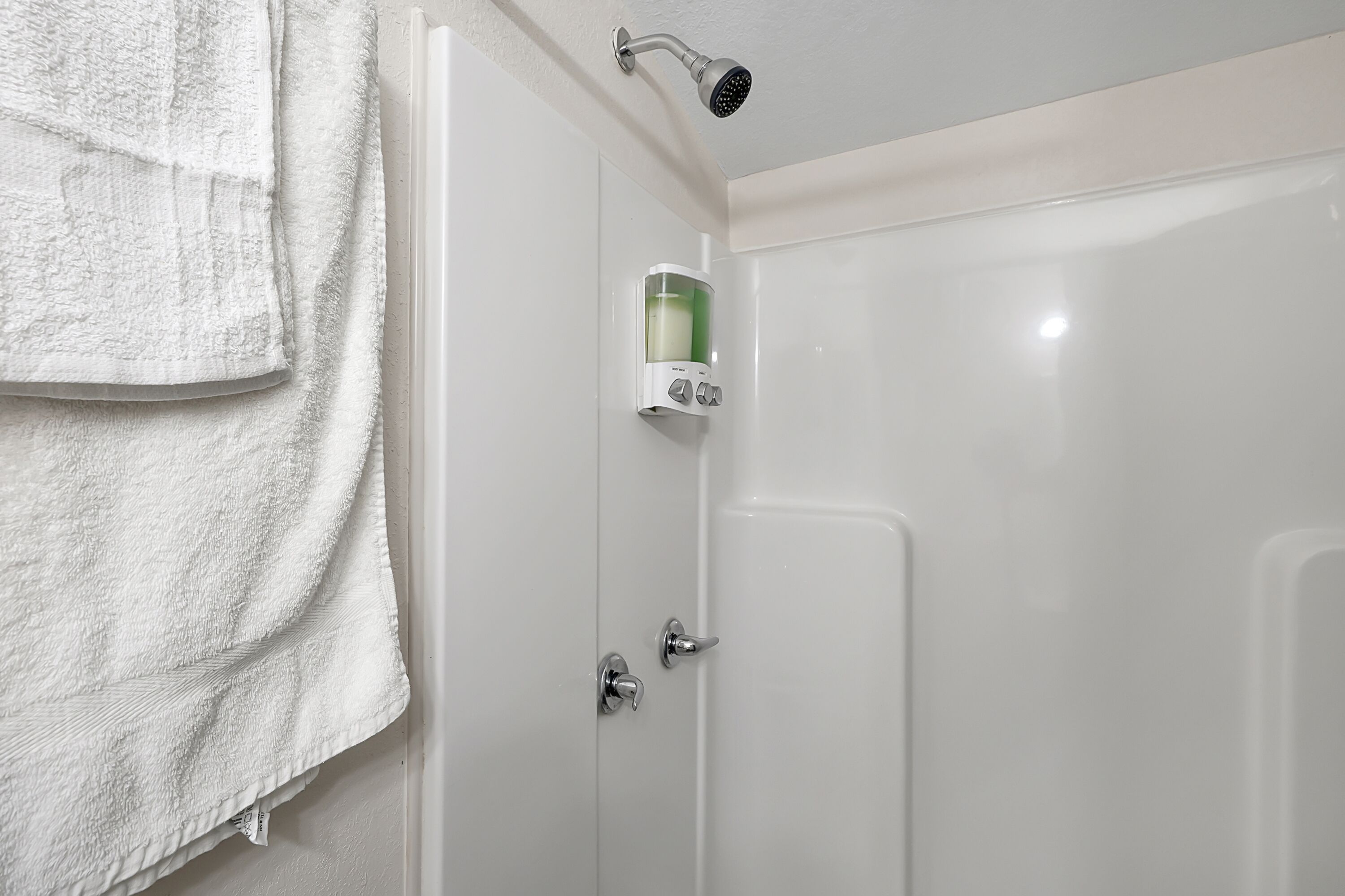A bathroom with a white shower, a towel rack, and a soap dispenser.