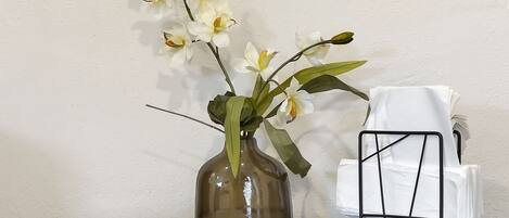 A glass table with a vase of white orchids, a black metal chair, and a stack of white napkins.