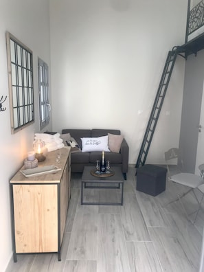 A modern living room with a wooden coffee table, a sofa, and a small side table with a bottle and glasses.