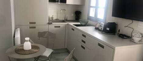A compact kitchen with a microwave, sink, and a small dining area with a chair and table.