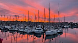 Un puerto deportivo con numerosos veleros amarrados, reflejándose en aguas tranquilas bajo un cielo de atardecer colorido.