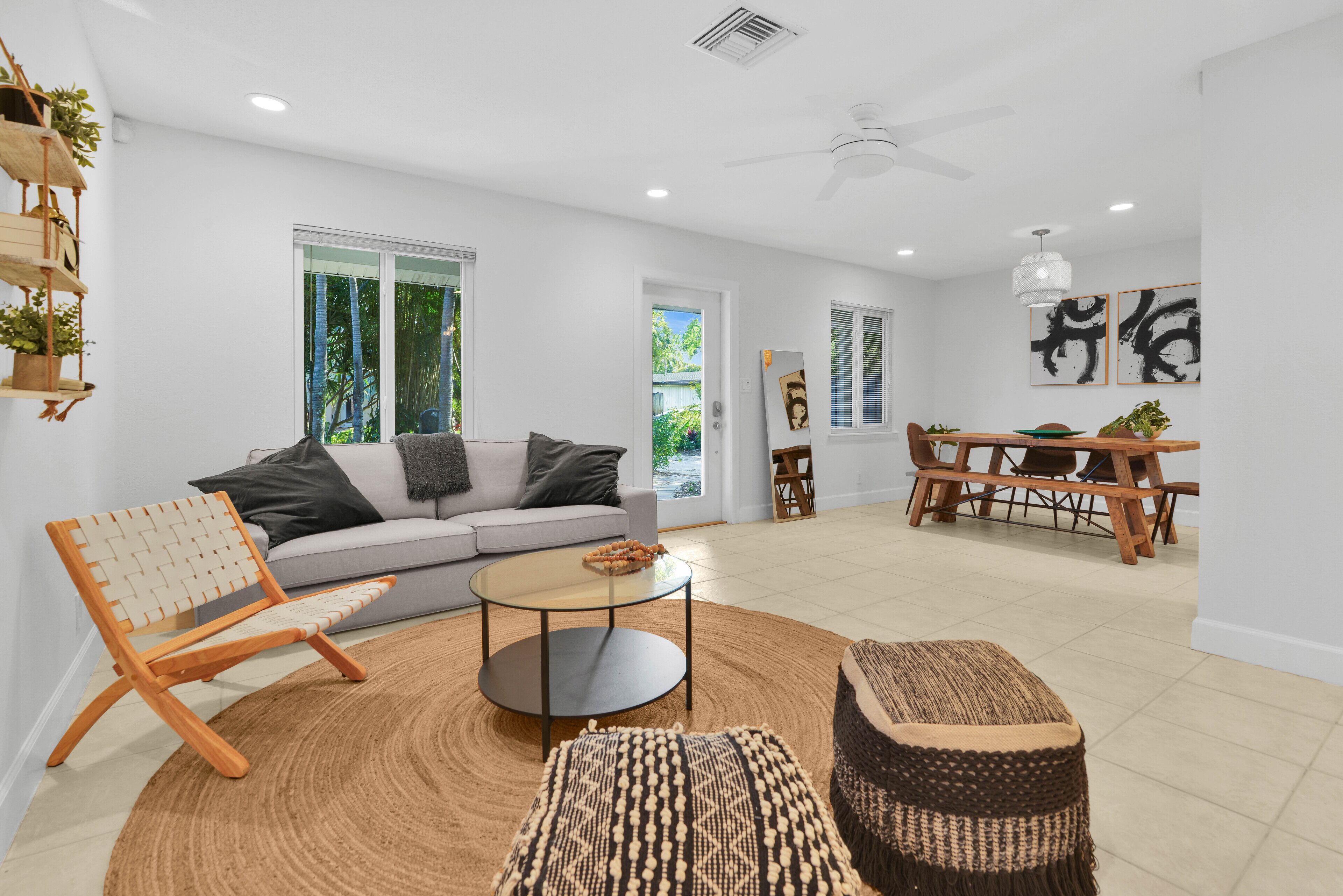 Ein modernes Wohnzimmer mit Sofa, Couchtisch und Hocker, sowie ein Essbereich mit Tisch und Stühlen und einem Deckenventilator.
