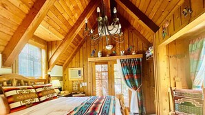Ein gemütliches Schlafzimmer in einer Holzhütte mit einem großen Bett, einer Deckenleuchte und einem Fenster mit Vorhängen.