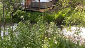 Eine Hütte mit Terrasse und Whirlpool, umgeben von dichtem Grün.