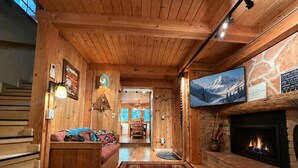 Ein Holzblockhaus-Interieur mit Kamin, einer Couch, einem Essbereich und einem an der Wand befestigten Fernseher.
