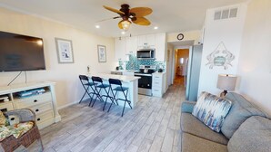 A compact living space with a kitchenette, a dining area with chairs, a sofa, and a television. - Coastal condo w. ocean views, community pool + beach access. (Tybee Island)
