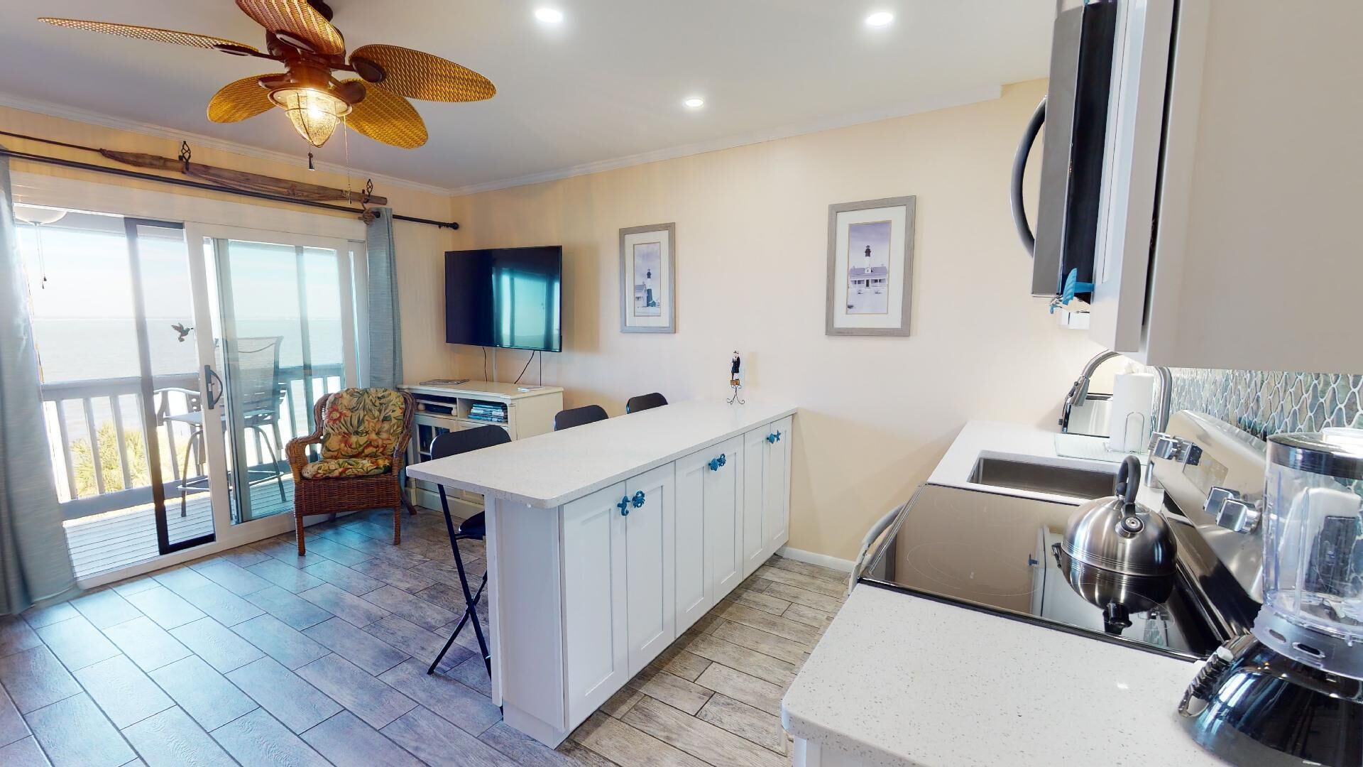 A modern kitchen with a central island, a dining area with a chair, a TV, and a balcony with a view.