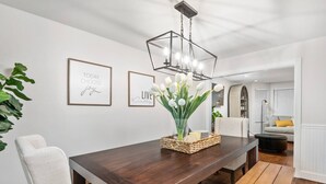 A dining area with a dark wooden table, white chairs, a chandelier, and framed inspirational quotes on the wall. - Sensationally Furnished *Hot Tub*, Pet Friendly, Game Room w/ Ping Pong, Foosball, Darts, Etc (Vancouver)