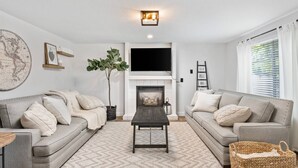 A living room with two grey sofas, a coffee table, a fireplace, a flat-screen TV, and a map on the wall. - Sensationally Furnished *Hot Tub*, Pet Friendly, Game Room w/ Ping Pong, Foosball, Darts, Etc (Vancouver)