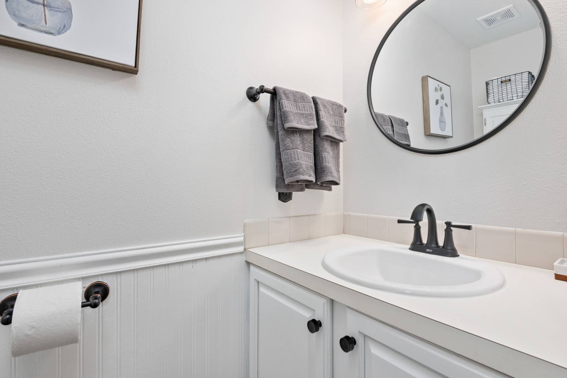 A bathroom with a white sink, a round mirror, and two towels hanging on a towel rack.