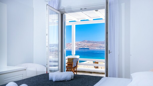 Une chambre d’hôtel avec un lit, une chaise, un bureau et vue sur la mer.