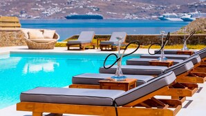 Un espace aménagé au bord de la piscine, avec des chaises longues et une vue sur la mer et les montagnes.