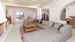 Un salon spacieux, doté d’un grand canapé d’angle, d’une table basse en bois et offrant une vue sur l’extérieur grâce à de grandes portes coulissantes.