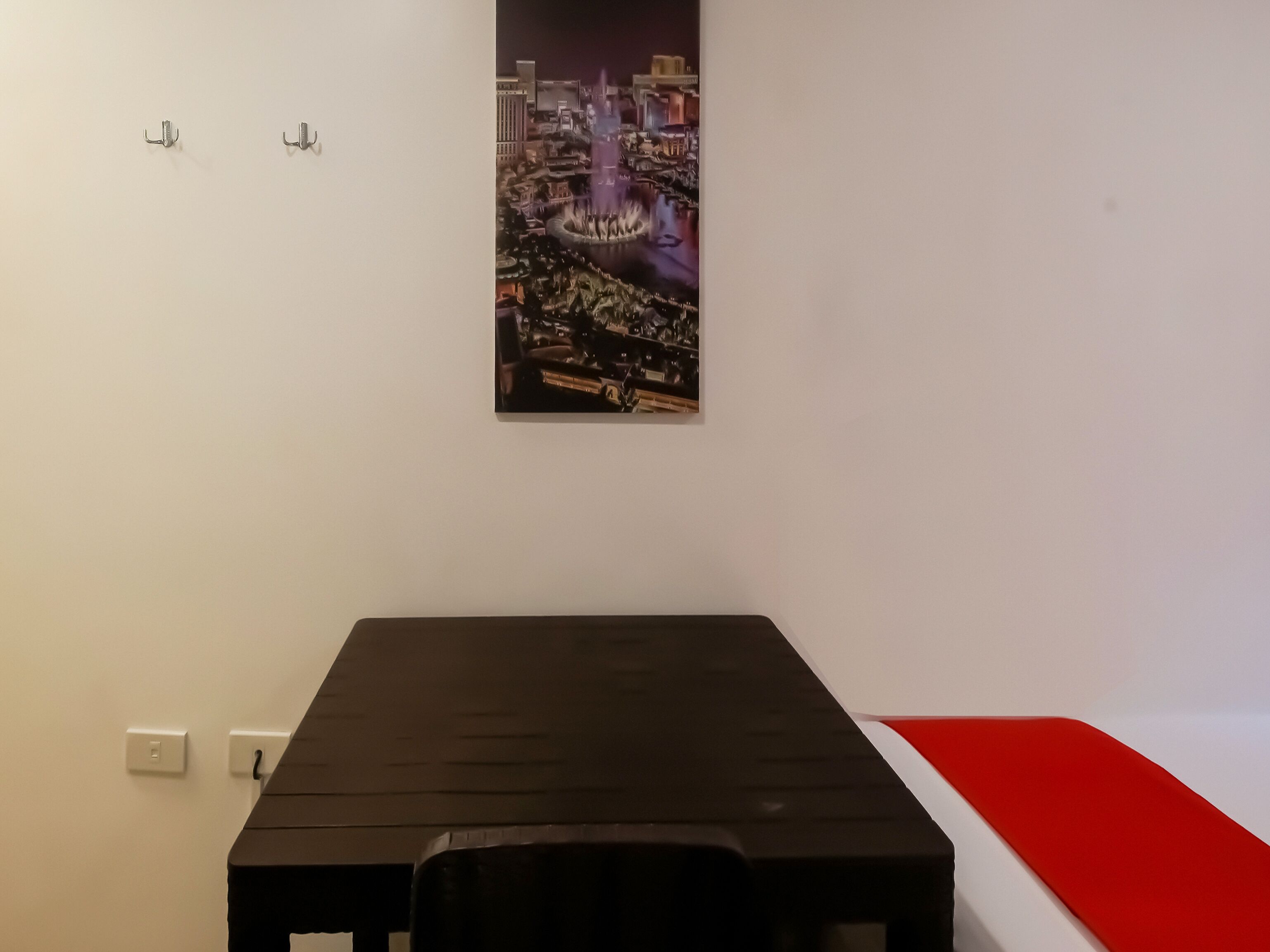 Une pièce avec une table noire, un banc rouge et un tableau représentant un paysage urbain accroché au mur.