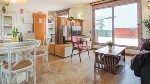 A spacious living area with a dining table, chairs, a sofa, and a TV. There is a sliding glass door leading to a balcony. - Atico Los Condes by Hello Homes Sitges (Sitges)