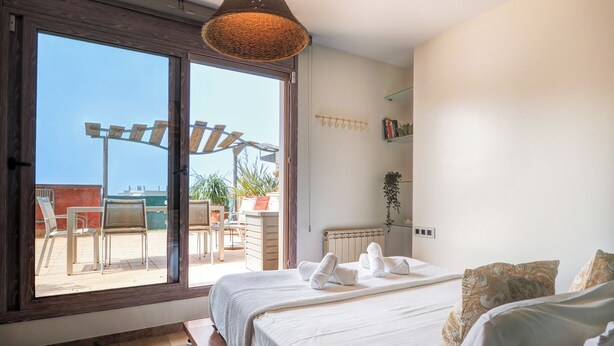 A bedroom with a large sliding glass door leading to an outdoor patio area, a bed with white linens, and a hanging woven light fixture. - Atico Los Condes by Hello Homes Sitges (Sitges)