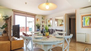 A dining area with a round table set for four, surrounded by white chairs with woven seats. - Atico Los Condes by Hello Homes Sitges (Sitges)
