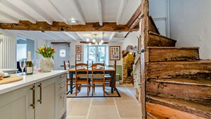A rustic kitchen with a wooden staircase, a dining area with chairs, and a stone fireplace. - Beautifully presented dog friendly holiday cottage in the Cotswolds with a courtyard garden - Heath (Stow-on-the-Wold)