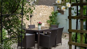 A garden patio with wicker furniture and a stone wall. - Beautifully presented dog friendly holiday cottage in the Cotswolds with a courtyard garden - Heath (Stow-on-the-Wold)