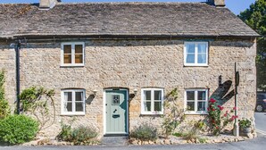 A stone house with a green door, two windows on the upper floor, and a chimney. - Beautifully presented dog friendly holiday cottage in the Cotswolds with a courtyard garden - Heath (Stow-on-the-Wold)