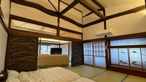 Una habitación japonesa tradicional con suelo de tatami, un futón, puertas correderas con paneles de shoji y un televisor sobre una mesita baja.