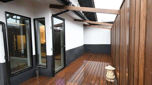 Un porche cubierto con suelo de madera, puertas de vidrio con marco negro y un muro de madera.