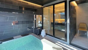 Un baño moderno con cabina de ducha de vidrio, un taburete blanco pequeño y un inodoro a la vista.