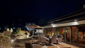 Un patio al aire libre con mobiliario de mimbre, una parrilla y una pérgola con luces colgantes.