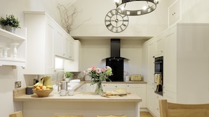 A modern kitchen with white cabinetry, a central island with stools, a black range hood, and a decorative clock. - The Staircase -  luxury dog friendly home in Stow on the Wold (Stow-on-the-Wold)