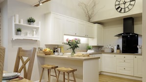 A modern kitchen with white cabinetry, a central island with stools, a coffee maker, and a clock on the wall. - The Staircase -  luxury dog friendly home in Stow on the Wold (Stow-on-the-Wold)