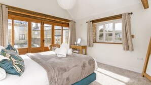 Een slaapkamer met een groot bed, houten balken, een bureau en uitzicht op een stenen gebouw.