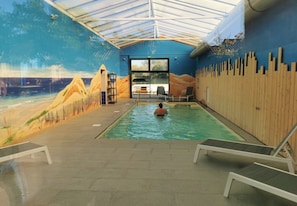 An indoor swimming pool with a mural of a beach scene, a wooden wall, and a person swimming.