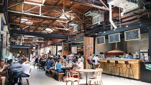 A bustling café with high ceilings, exposed beams, and a mix of seating options including tables and bar stools. - Cozy Studio Bungalow Walk to Armature and Downtown (Tampa)