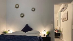 A bedroom with a bed, bedside tables, wall-mounted lights, and a small plant. - Cozy Studio Bungalow Walk to Armature and Downtown (Tampa)