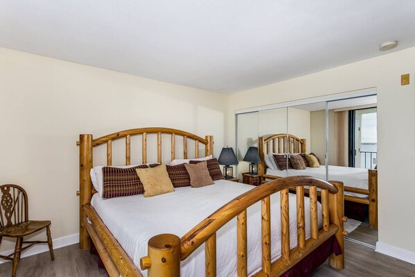 A bedroom with a wooden bed, a chair, a nightstand with lamps, and a large mirror.