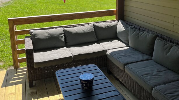 A covered outdoor seating area with a wicker sofa and a table, overlooking a grassy landscape with an American flag.