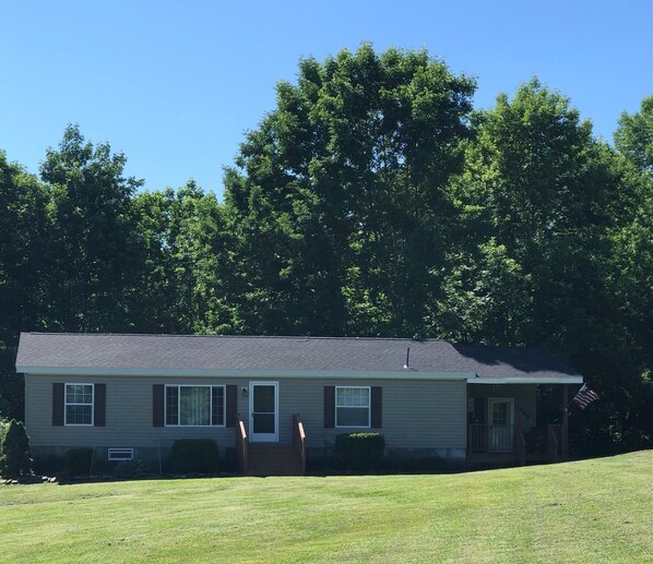 A single-story house with a front porch, a small front yard, and a flagpole with an American flag.