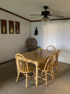 A dining room with a wooden table and four chairs, a ceiling fan, and three wall-mounted decorations.