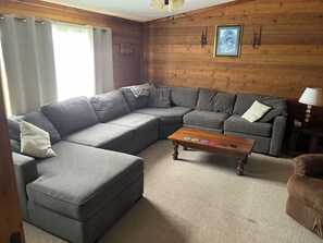 A living room with a sectional sofa, a coffee table with colorful objects, and a lamp.